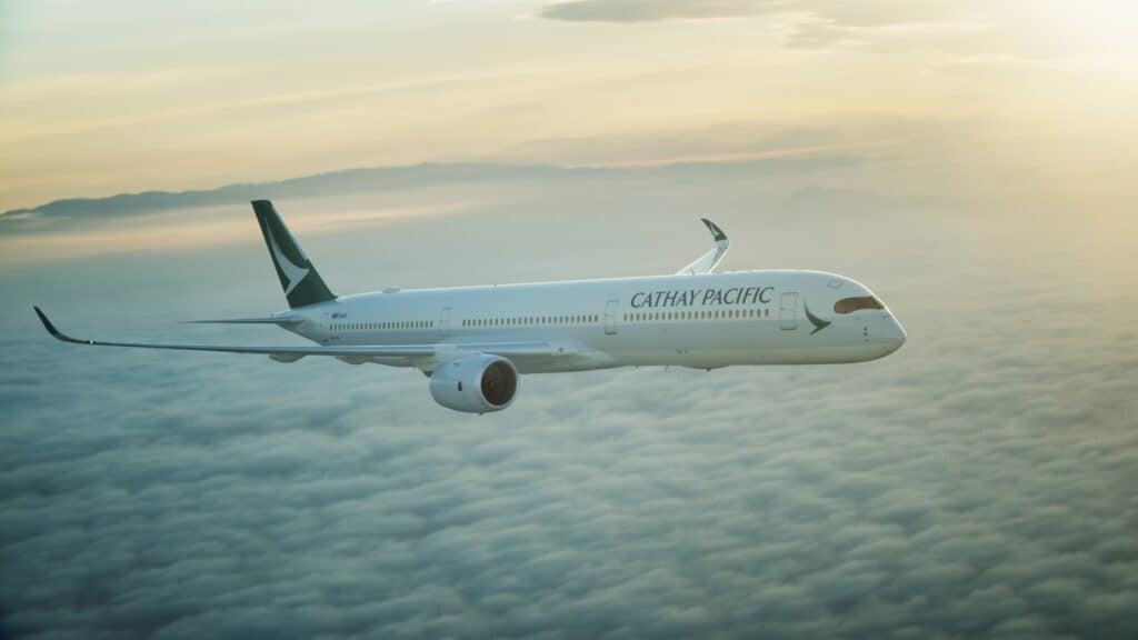 Cathay Pacific airplane flying above clouds during sunset with mountains visible in the background.