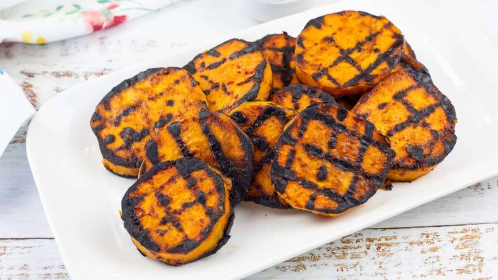 Grilled sweet potato slices with visible char marks arranged on a white rectangular plate.