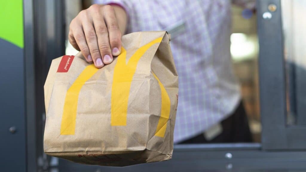 A person hands a McDonald's paper bag out of a drive-thru window.