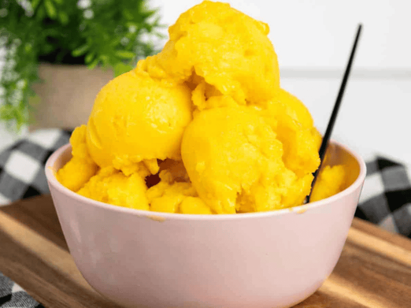 A bowl of mango sorbet on a wooden table.