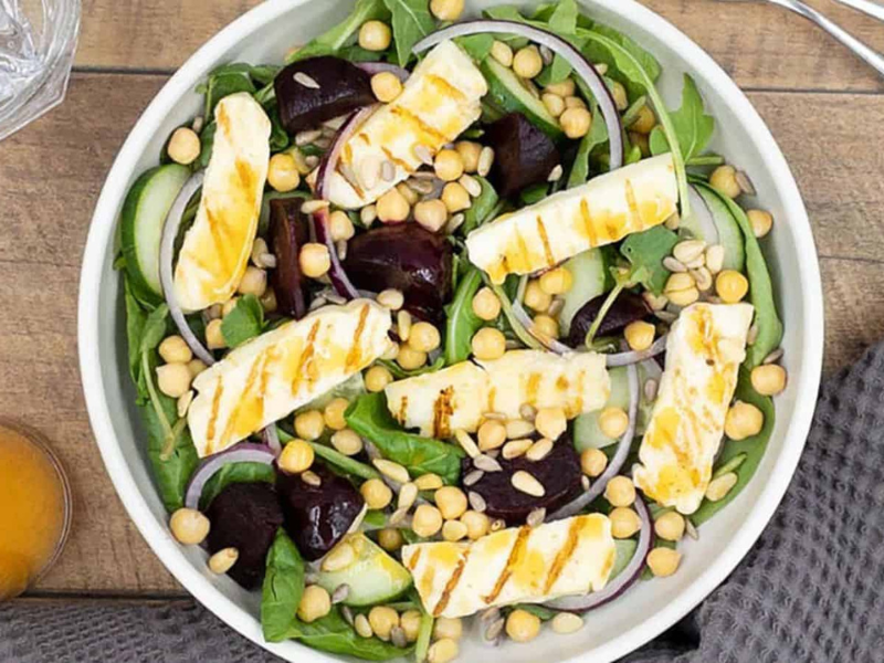 Sliced halloumi cheese, beets and greens in a white ceramic bowl.
