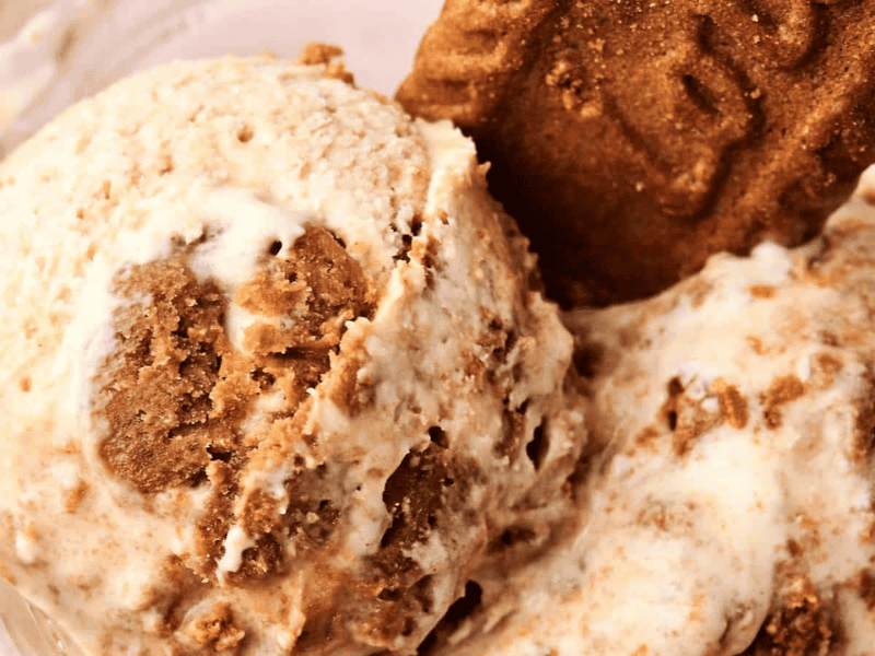 Scoops of ice cream with chunks of cookie and a whole cookie piece placed on top in a glass bowl.