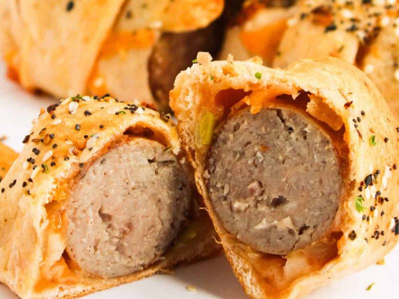 Sliced sausage wrapped in golden-brown pastry, sprinkled with sesame and poppy seeds.