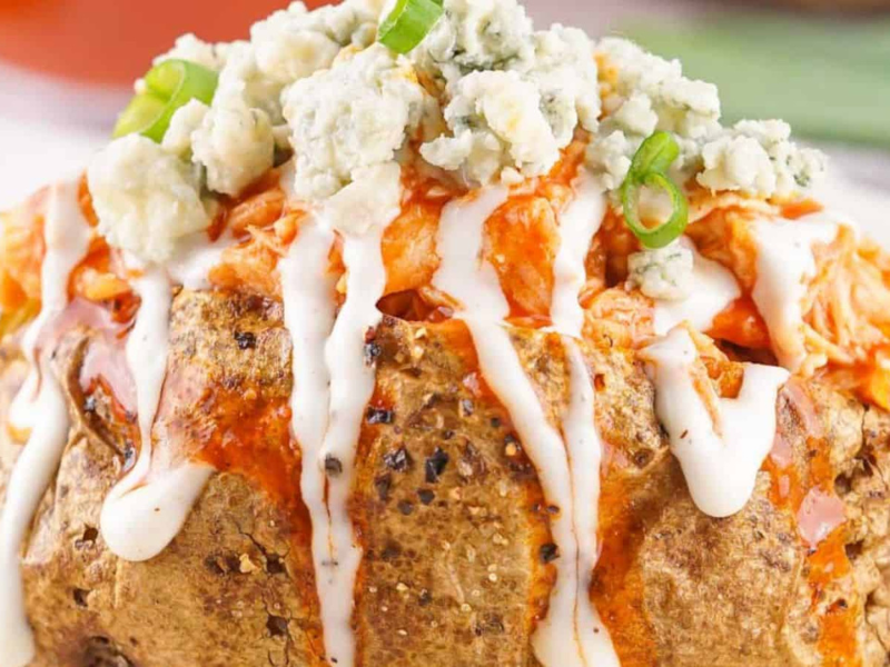 Buffalo Chicken Baked Potatoes topped with blue cheese, drizzled with ranch dressing, and garnished with green onions.