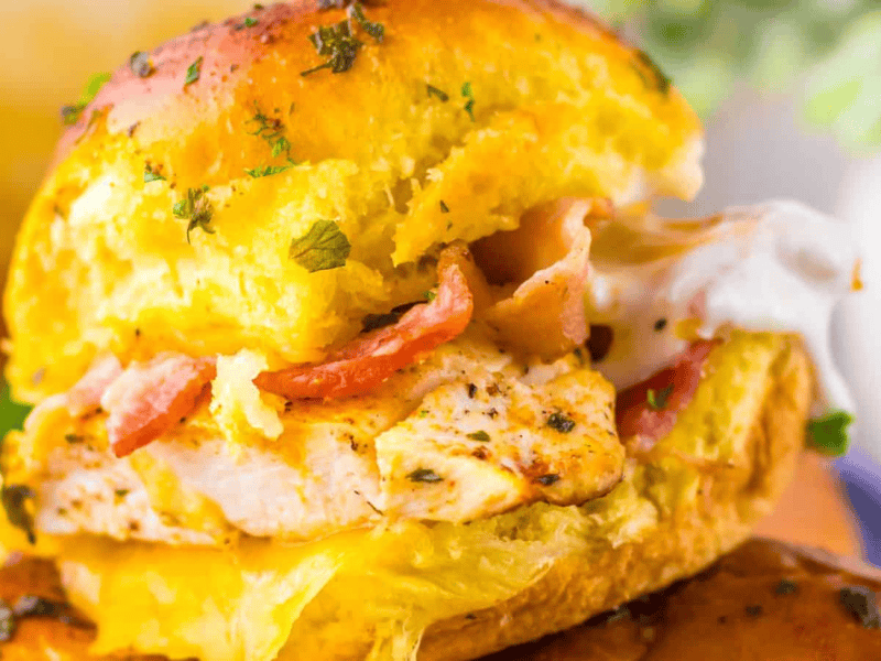 Close-up of chicken bacon ranch sliders with grilled chicken, bacon, and melted cheese inside a golden bun, garnished with herbs.