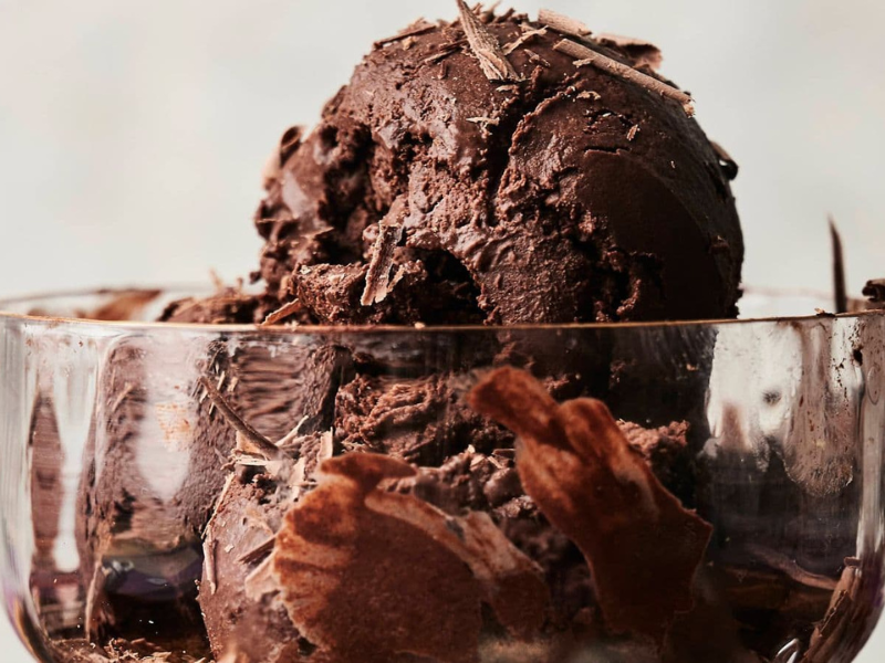 A glass bowl filled with scoops of dark chocolate ice cream topped with chocolate shavings.