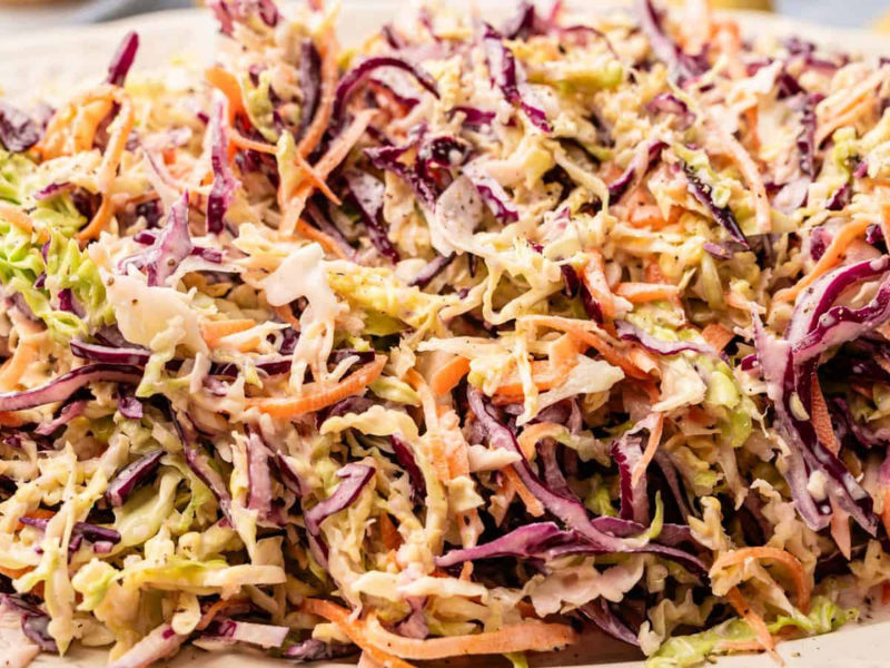 A close-up of coleslaw made with shredded green and purple cabbage, carrots, and creamy dressing on a white plate.