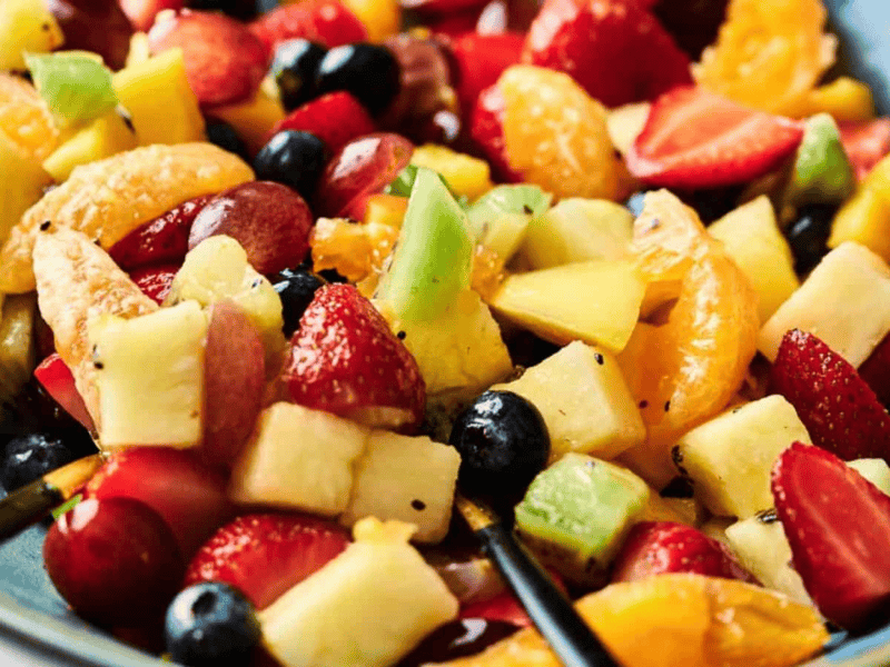 Fruit salad in a blue bowl with a spoon.
