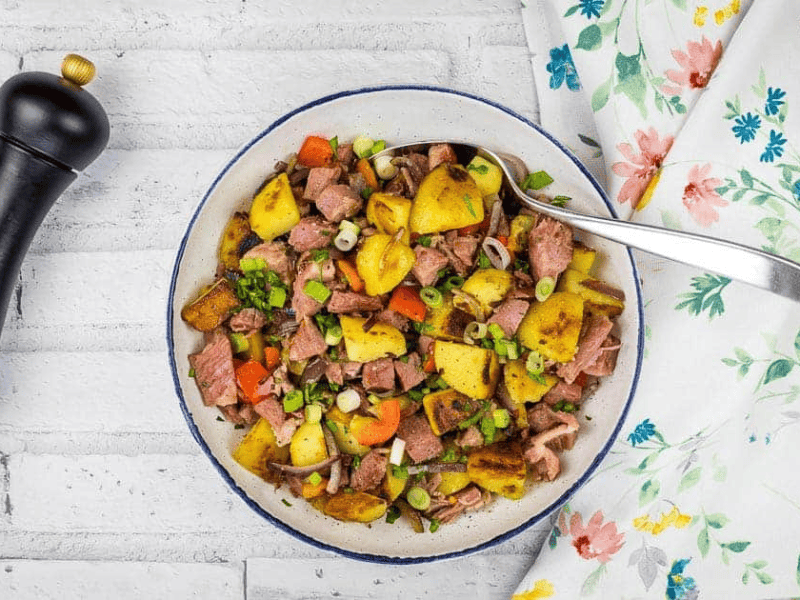 A bowl of leftover cottage roll hash on a white tablecloth.