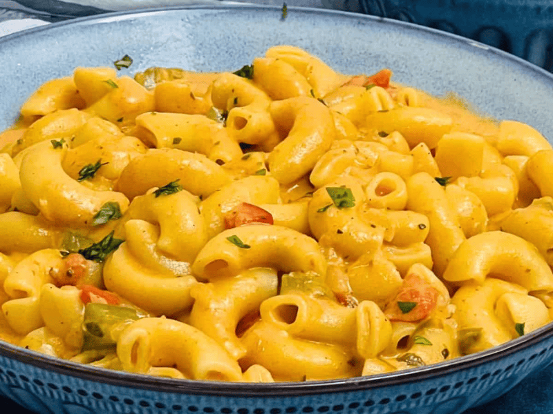 A bowl of creamy Masala Mac and Cheese with chopped herbs, served in a blue dish.