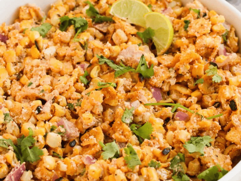A bowl of Mexican street corn salad garnished with lime wedges and cilantro.