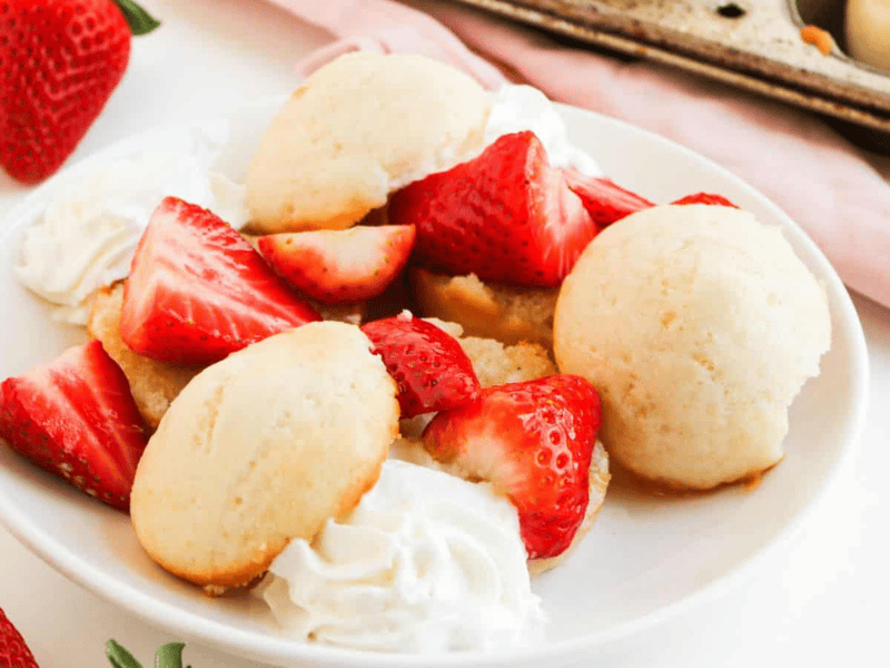 A plate of strawberry shortcake with sliced strawberries, dollops of whipped cream, and small round shortcakes on a white plate.