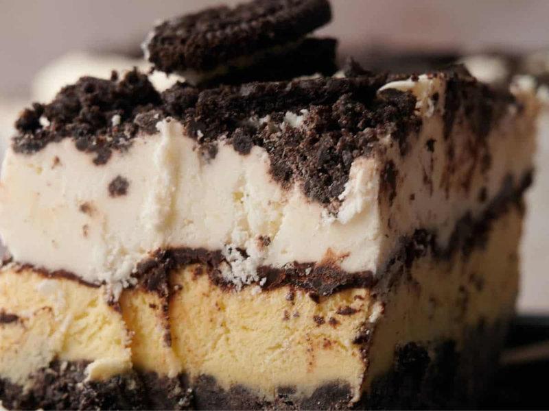 A slice of layered ice cream cake with chocolate cookie crumbles and a cookie on top, served on a plate.