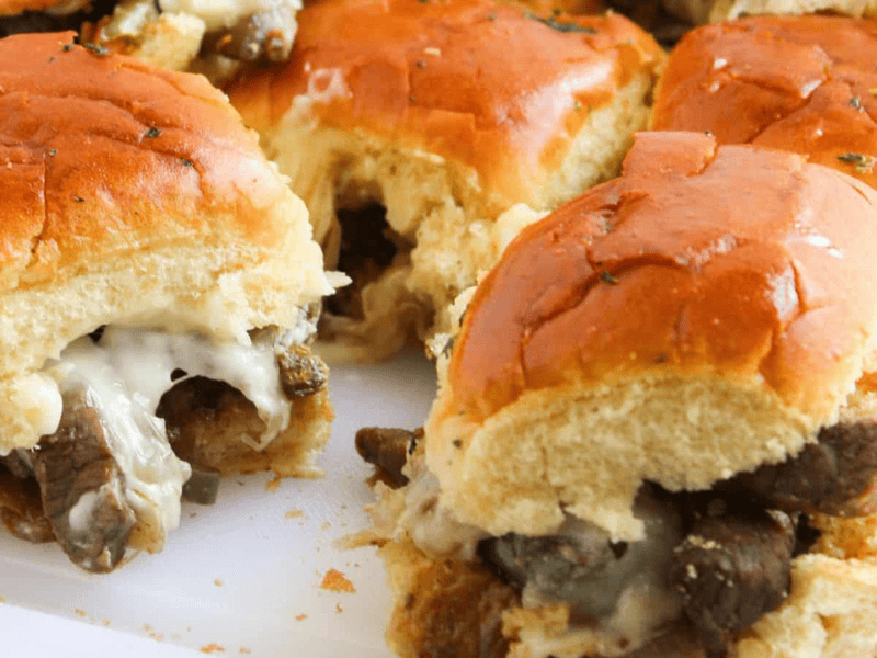 Close-up of beef and cheese sliders with toasted buns on a white surface.