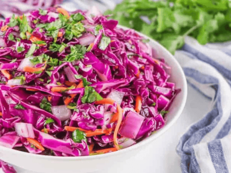A bowl of fresh red cabbage coleslaw garnished with herbs.