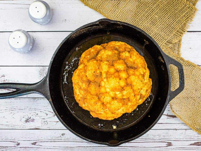 Smoked cauliflower in a skillet on a wooden table.