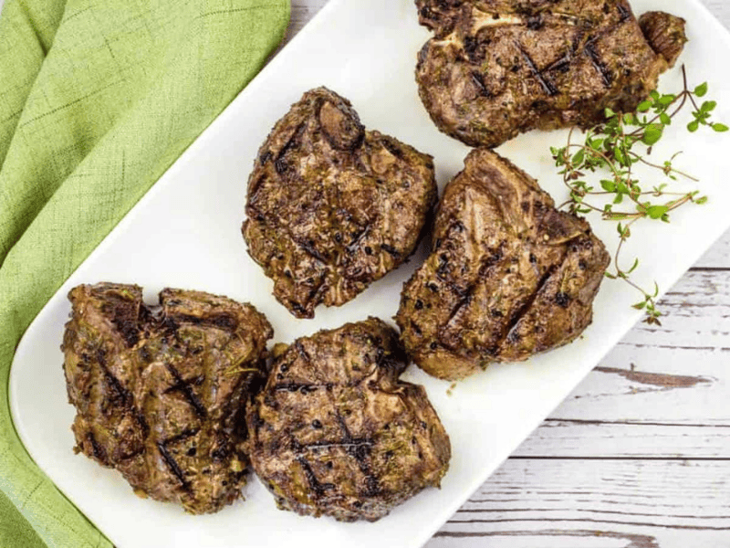 Smoked lamb chops on a white plate with a green napkin.