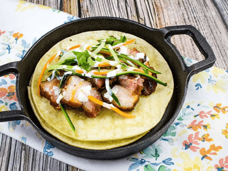A closeup shot of two tacos filled with smoked pork belly and vegetables.
