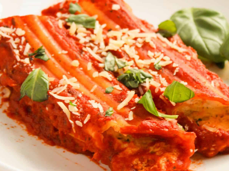 A plate of stuffed cannelloni topped with tomato sauce, grated cheese, and fresh basil.