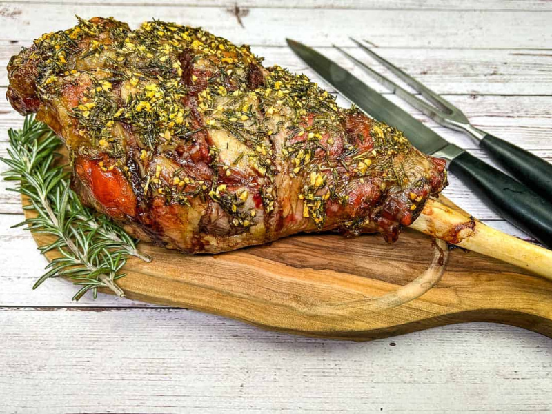 Whole cooked leg of lamb on a board with a knife.