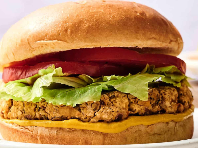 A close-up of a veggie burger with a plant-based patty, lettuce, tomato slices, and mustard in a sandwich bun.