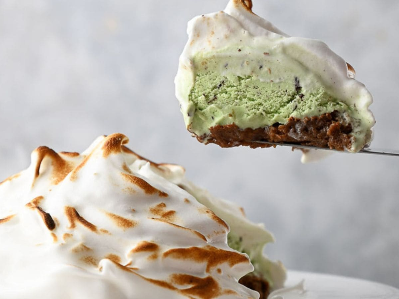 A slice of baked Alaska with a toasted meringue exterior and green ice cream center being lifted from the dessert.