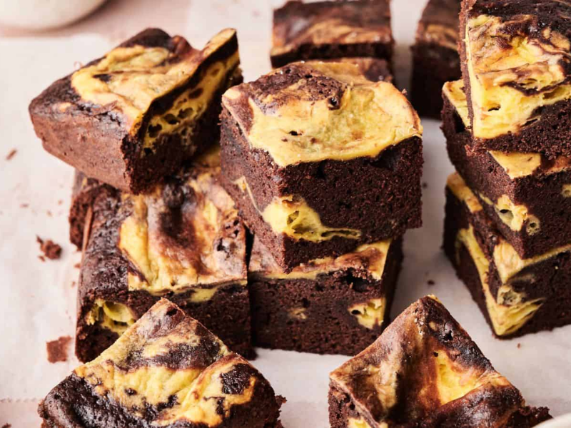 Several squares of chocolate brownies with a yellow and brown marbled pattern are stacked and arranged on parchment paper.