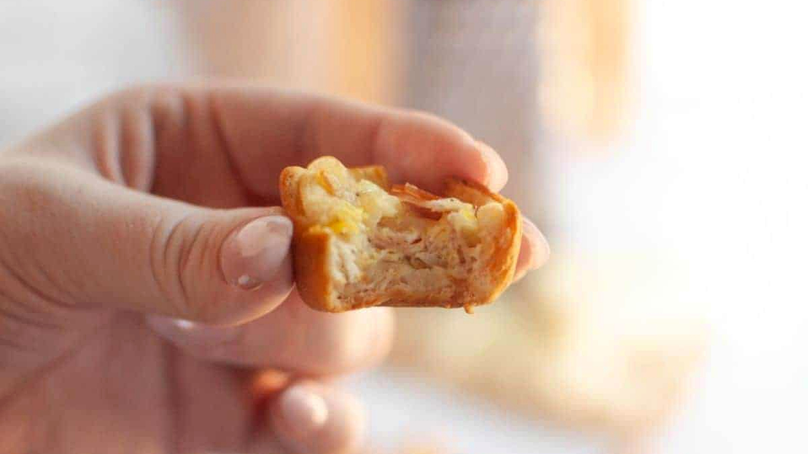 A hand holds a partially eaten Ham and Cheese puff, revealing layers of pastry, ham, and cheese.