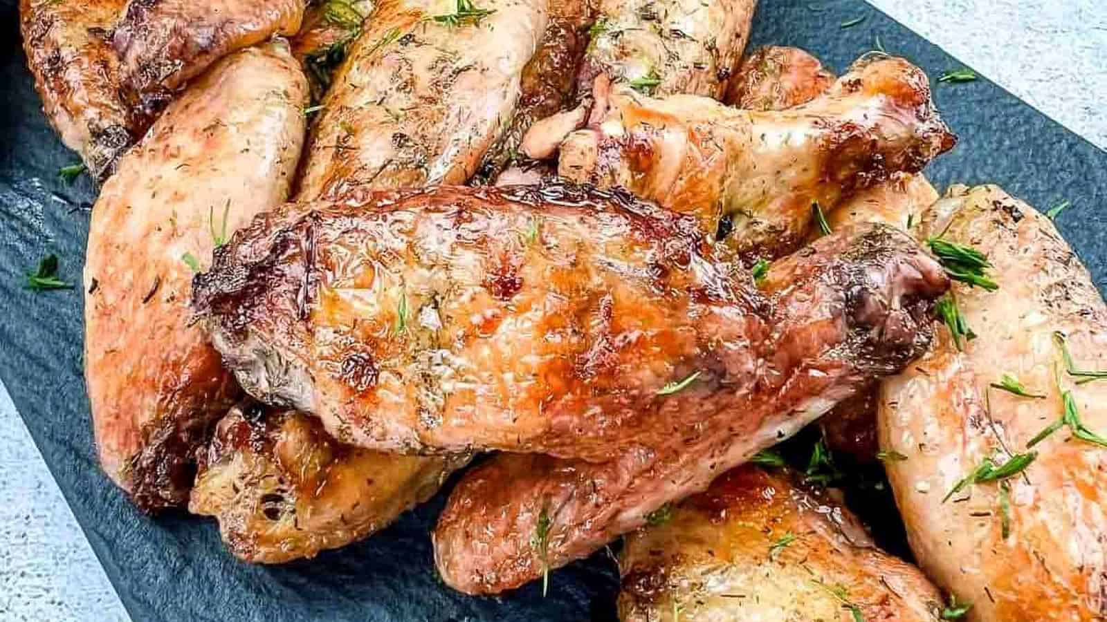 Smoked chicken wings with pickles on a black plate.