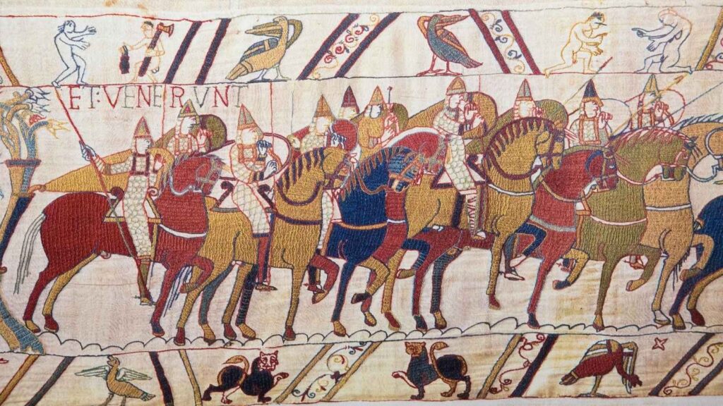 A scene from the Bayeux Tapestry showing armored soldiers on horseback, carrying spears and shields, with decorative borders featuring animals and birds.