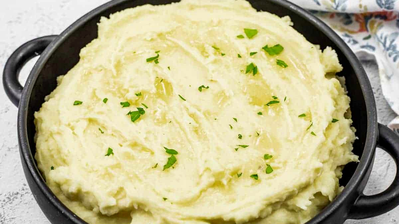 Mashed potatoes with cream cheese topped with melted butter and garnished with fresh parsley.