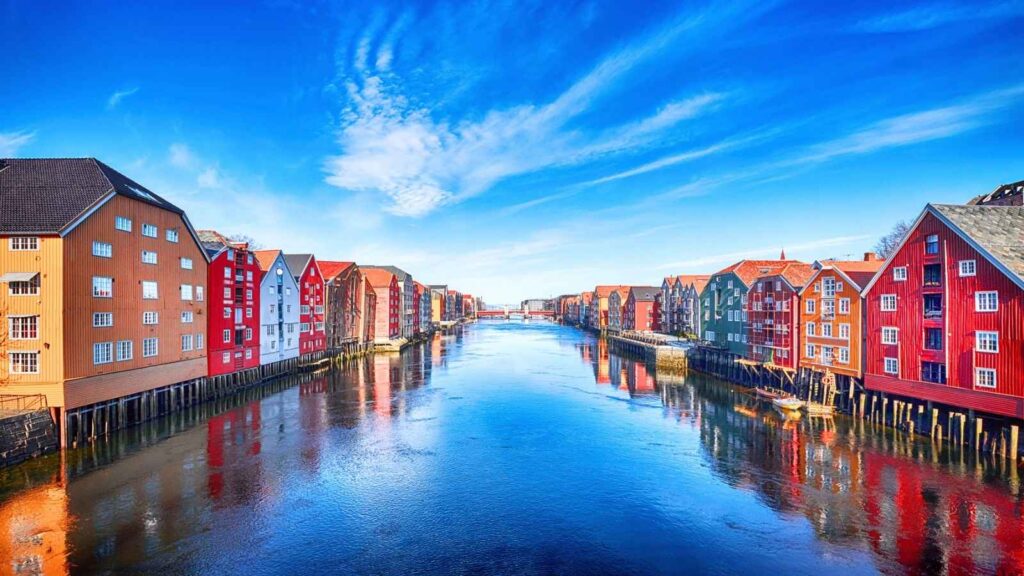 Colorful wooden buildings line both sides of a calm river under a blue sky with wispy clouds, evoking the charm of Arctic Norway&mdash;where even a Michelin star restaurant could feel at home.