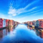 Colorful wooden buildings line both sides of a calm river under a blue sky with wispy clouds, evoking the charm of Arctic Norway—where even a Michelin star restaurant could feel at home.