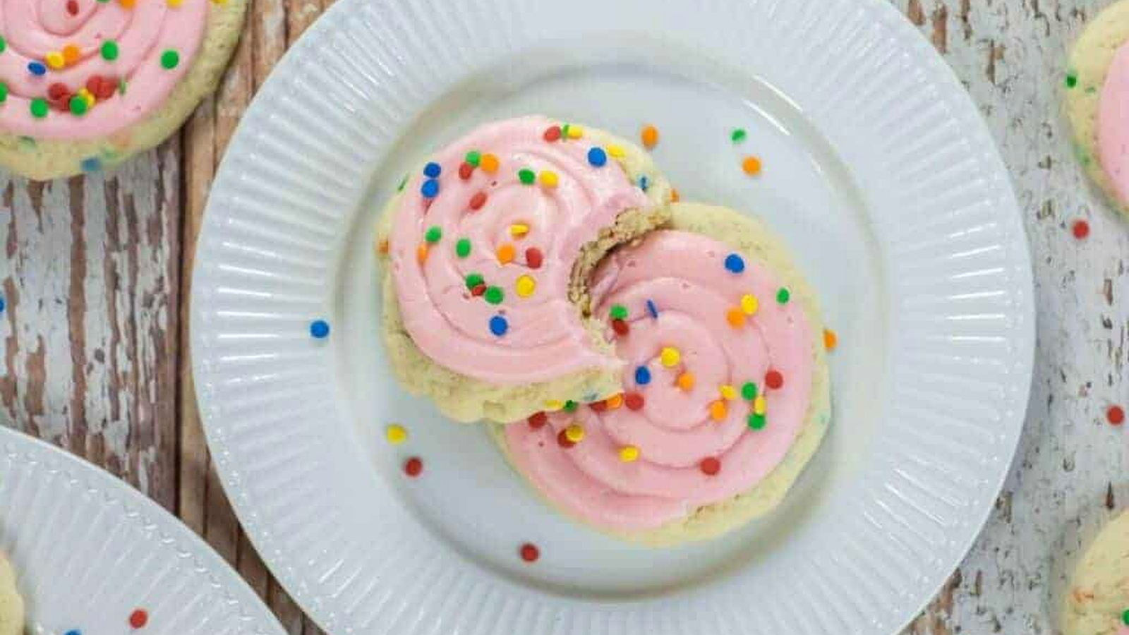 Two Crumbl-Style Confetti Cake Cookies on a white plate; one cookie has a bite taken out of it.