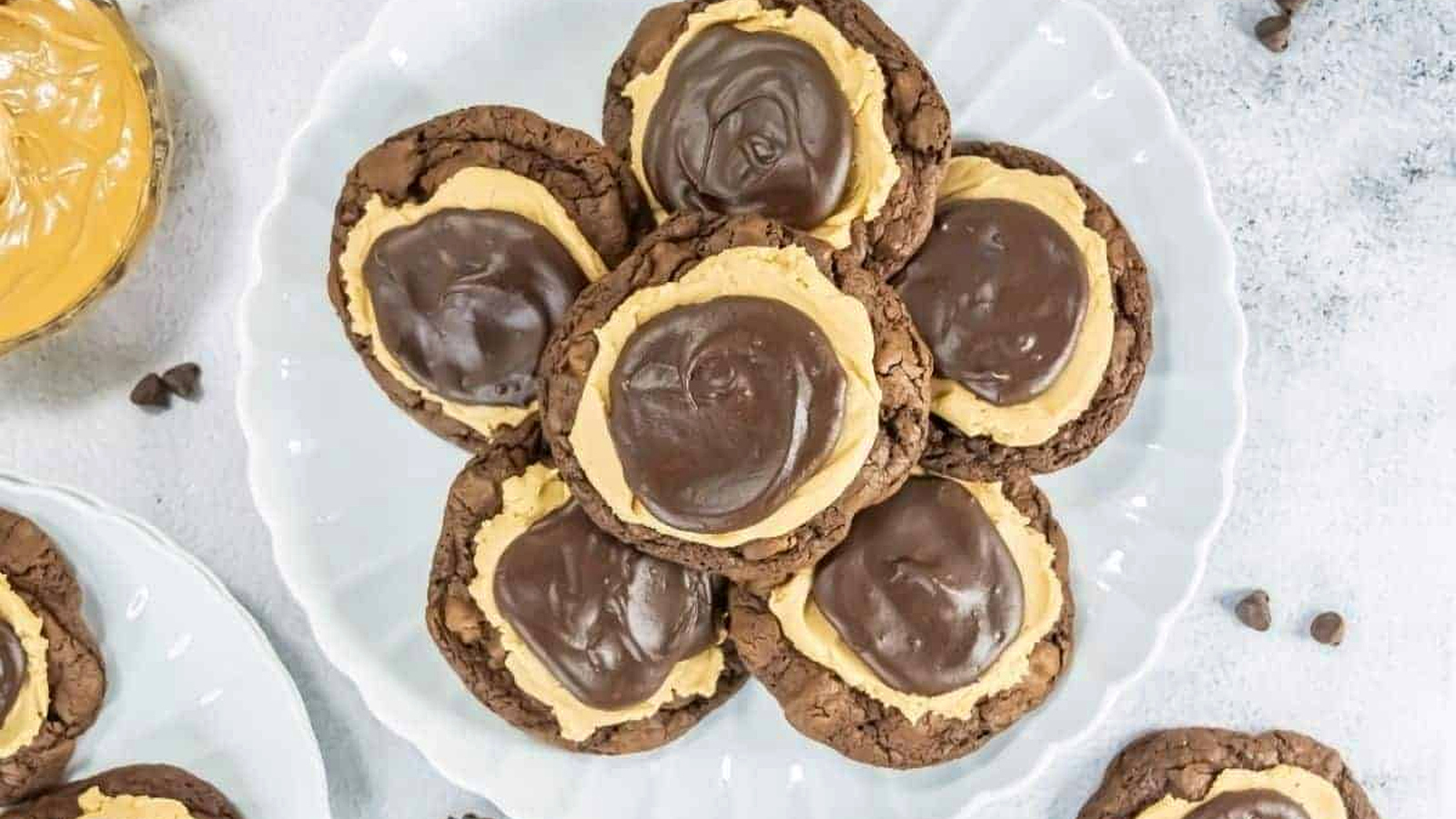 A white plate holds several chocolate cookies topped with a layer of peanut butter and a swirl of chocolate frosting.