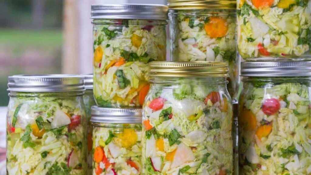 Several glass jars filled with colorful chopped vegetables, such as cabbage, carrots, and peppers, are stacked on a surface, ready for pickling or storage.