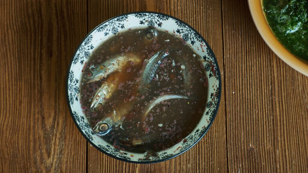 A bowl with whole fish in a dark broth, enriched with ancient Roman garum, placed on a wooden surface.