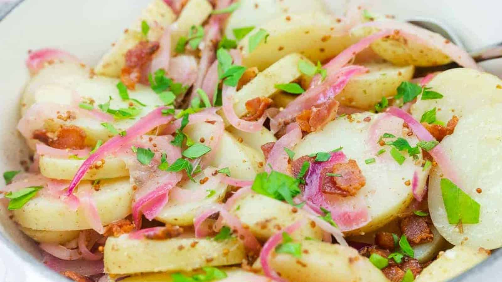 Chef Jenn&rsquo;s Warm German Potato Salad with sliced potatoes with bacon, red onions, and chopped parsley, served in a white bowl.