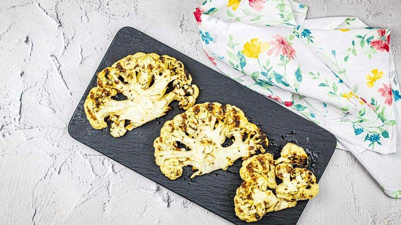 Three pieces of grilled cauliflower steaks on a black plate.