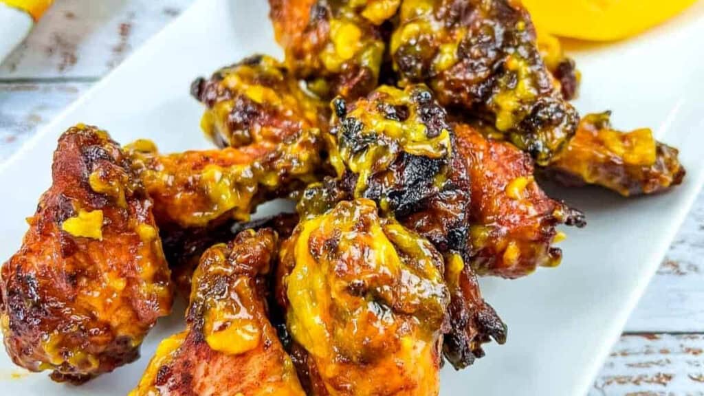 Plate of cooked chicken wings coated in a yellow and brown sauce, served on a white rectangular dish.