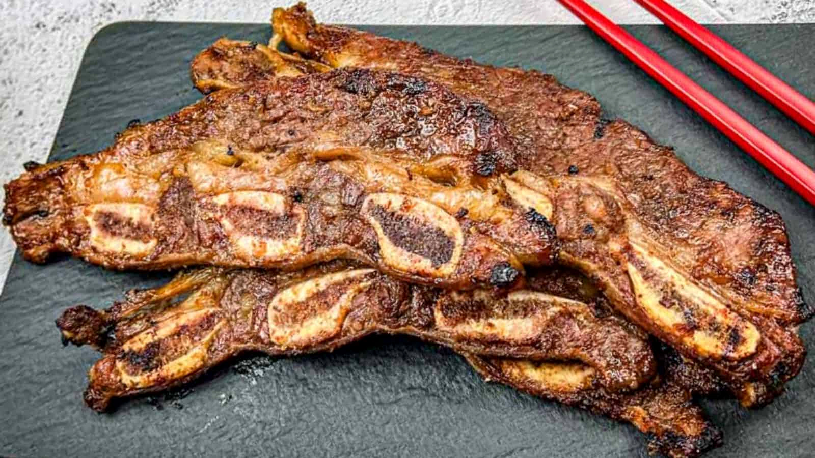 Korean Galbi Ribs on a slate platter with red chopsticks beside them.