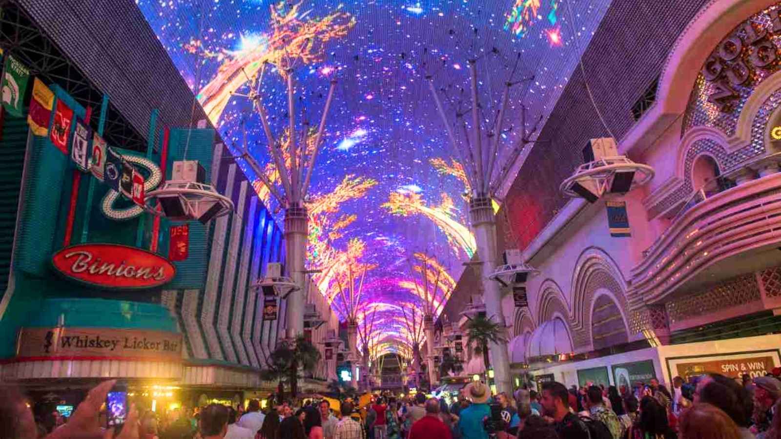 A crowd gathers under a brightly lit, colorful digital canopy at the Fremont Street Experience in Las Vegas at night.