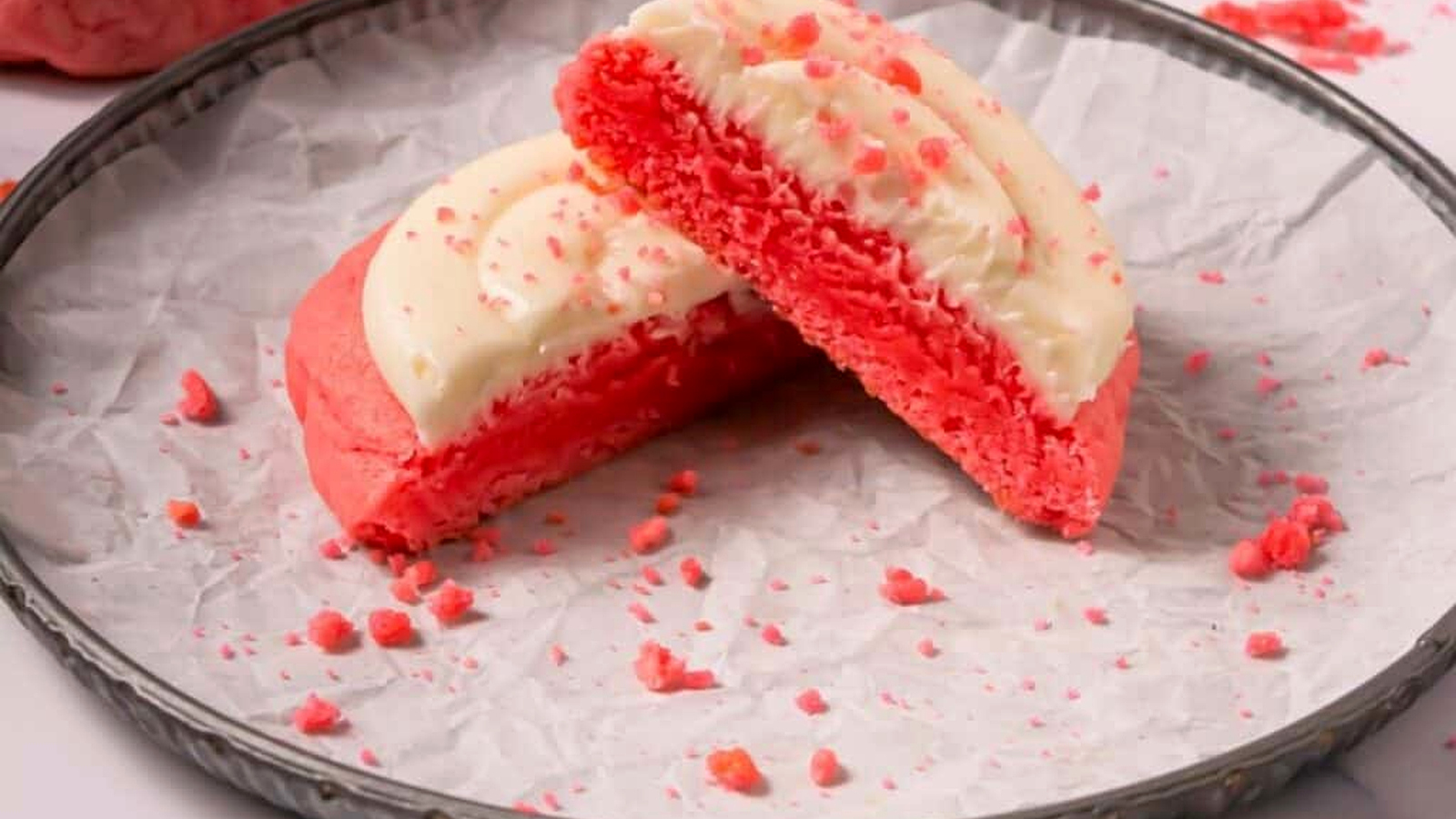 A Crumbl Copycat Pink Velvet Cookies is cut in half and displayed on a round metal tray lined with crinkled parchment paper.
