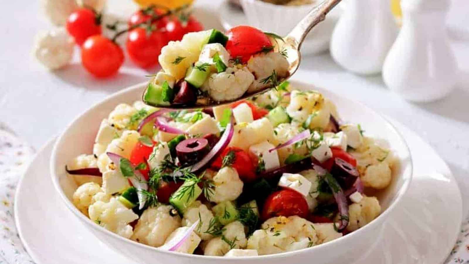 A spoon holds a serving of Greek Cauliflower Salad above the bowl.