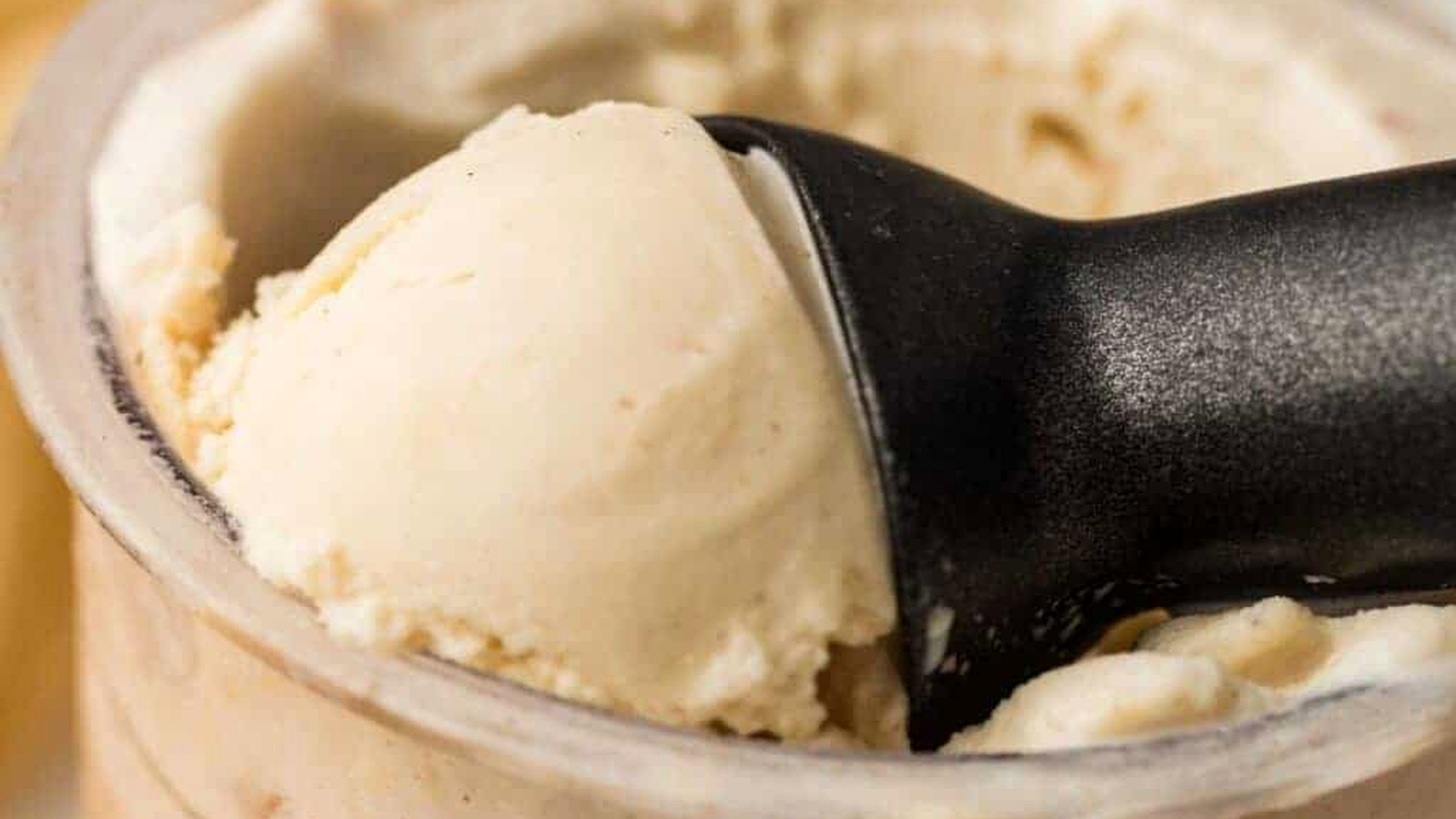 A close-up of a black ice cream scoop lifting vanilla ice cream from a container.