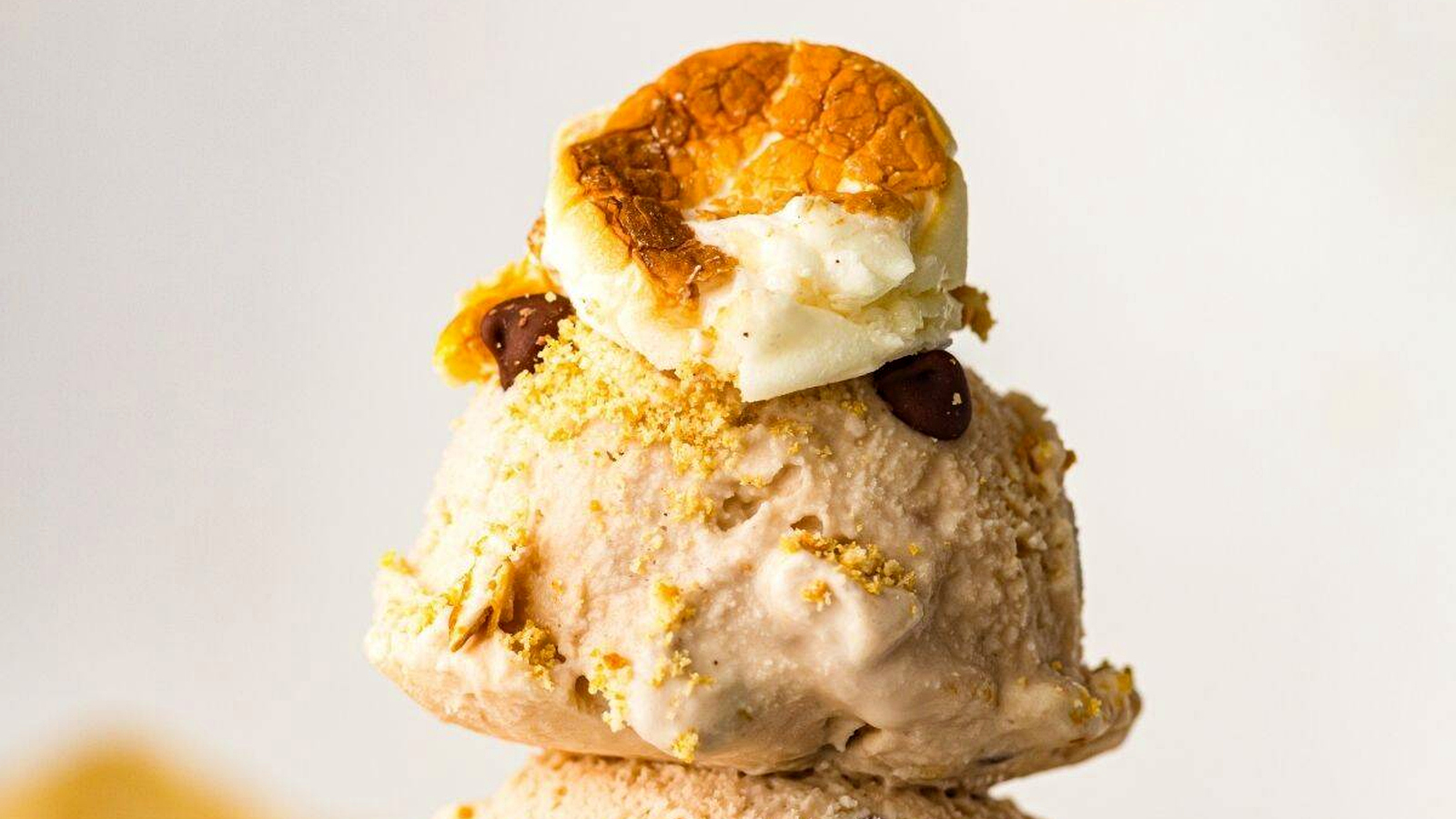 A scoop of S&rsquo;mores  ice cream topped with crushed graham crackers, chocolate chips, and a toasted marshmallow.