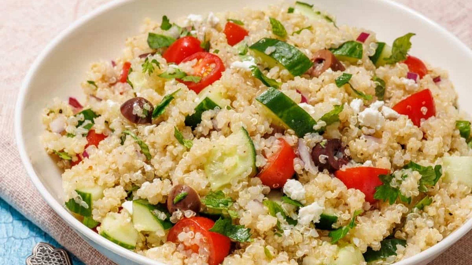 A white bowl of Mediterranean Quinoa Salad on a light blue tablecloth.