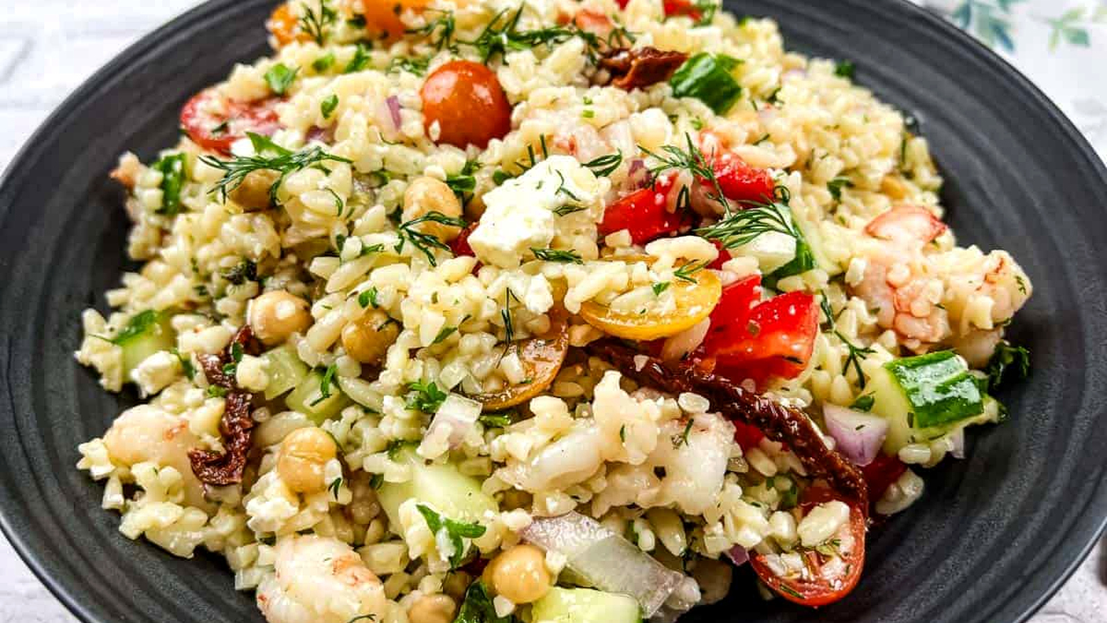A bowl of Mediterranean orzo salad on a black plate.