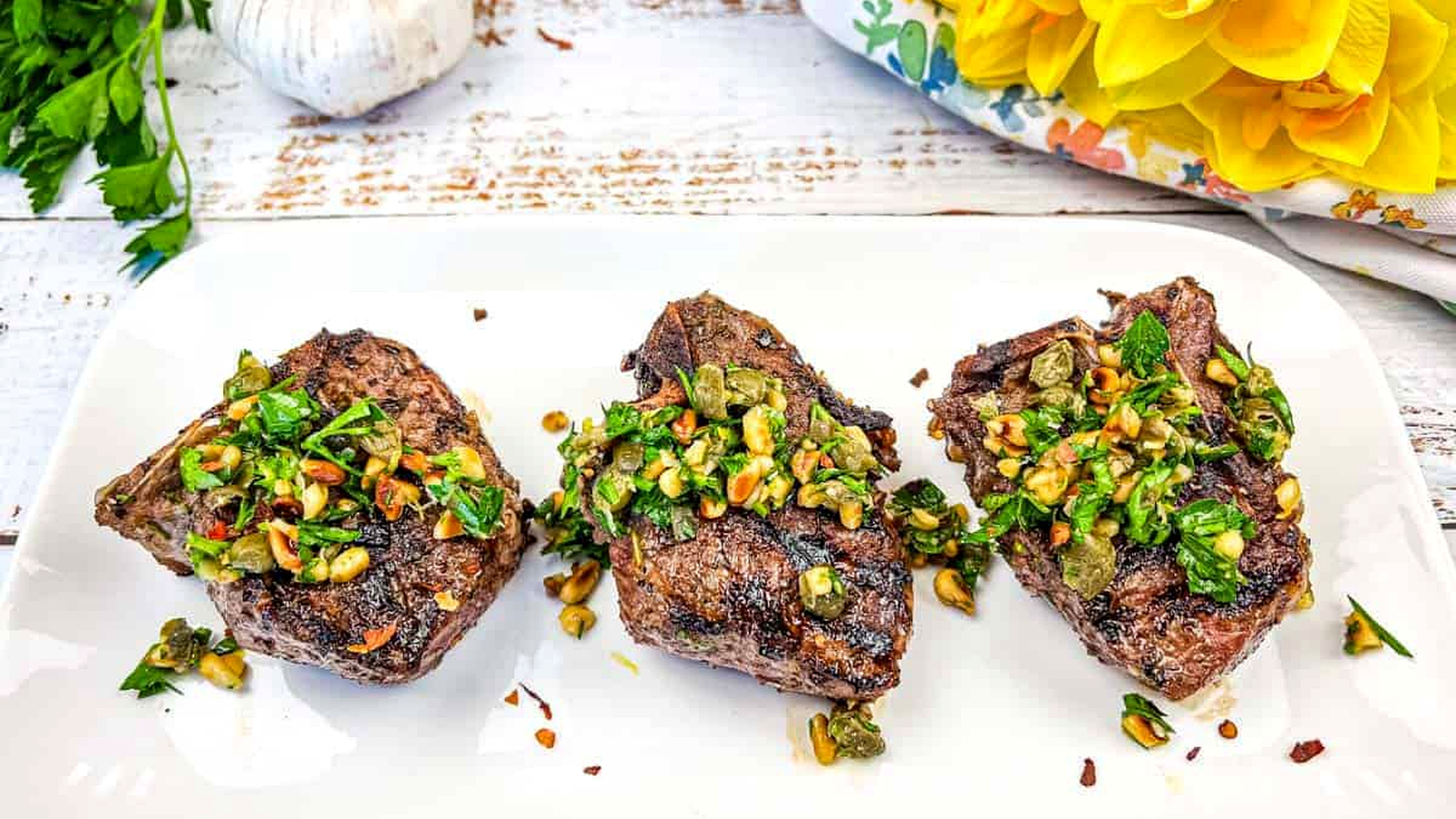 Three Grill Mediterranean Lamb Chops topped with gremolata on a white plate.