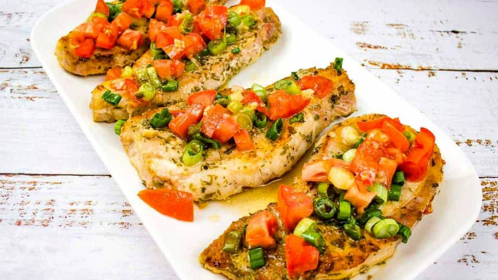 Three pork chops with tomato and green onion on a white plate.